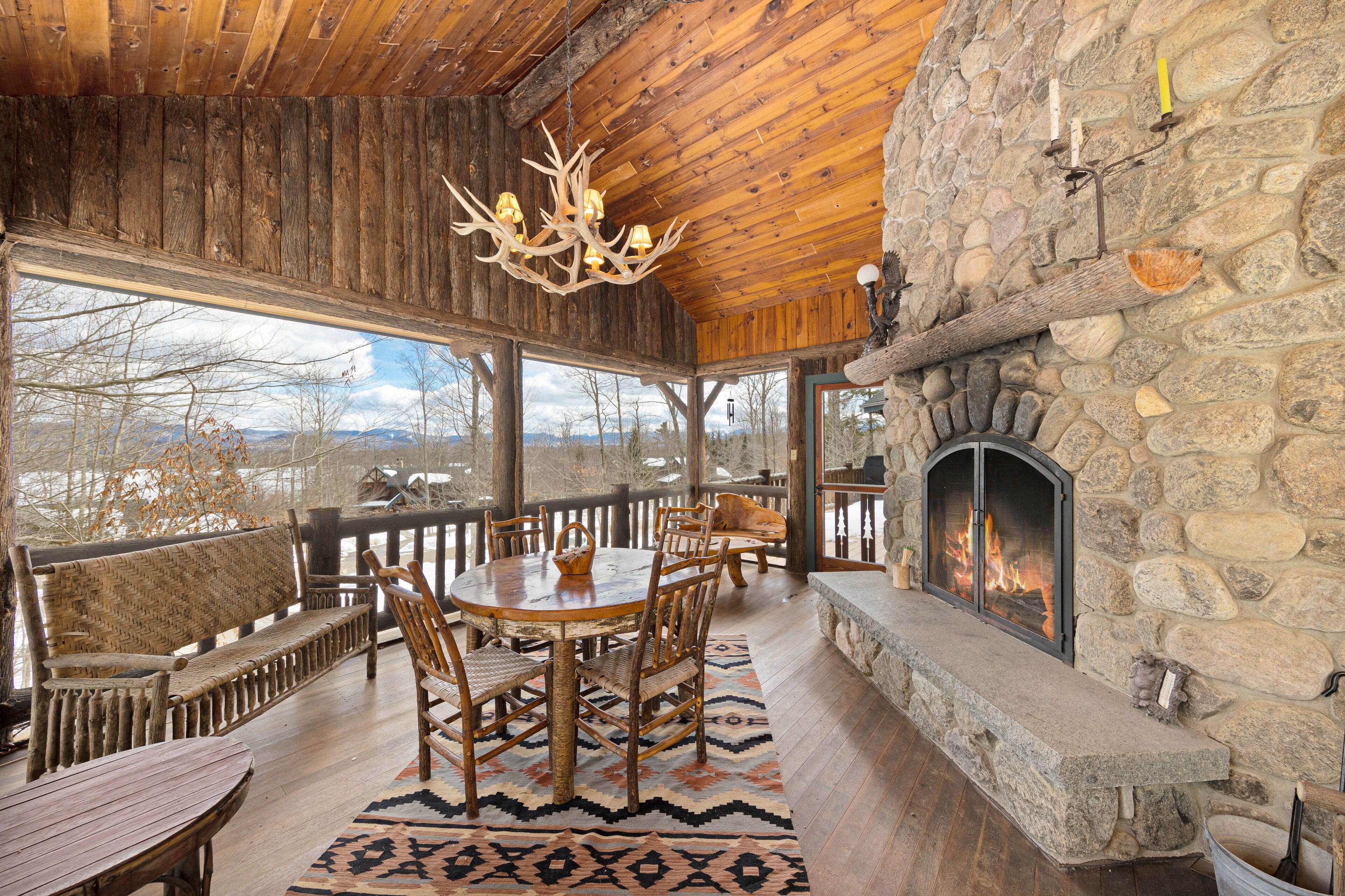 Un intérieur rustique avec des éléments en bois, une cheminée en pierre, des meubles en bois et une vue sur l’extérieur.