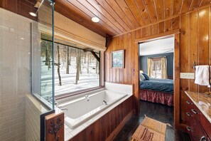 Een houten blokhut met een vrijstaand bad, een houten wastafel en een bed met een rode dekbedovertrek.