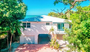 A white house with a garage, surrounded by lush greenery and a clear blue sky.