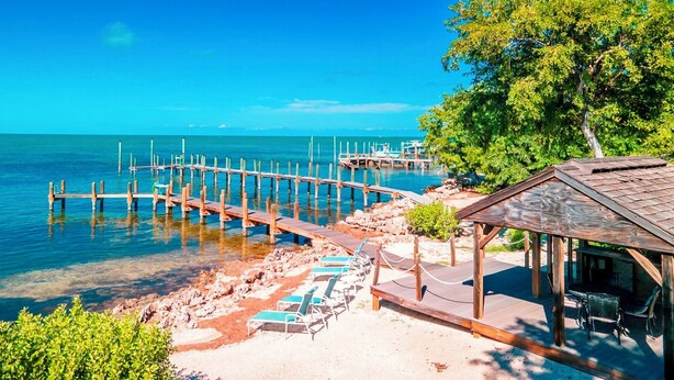 A beach with wooden piers, clear blue water, and a small pavilion with a roof.