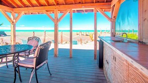 A wooden deck with a table and chairs, overlooking a beach.