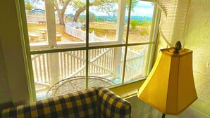 Una habitación con un sofá a cuadros, una mesa con lámpara y una ventana que da a un espacio exterior cercado.