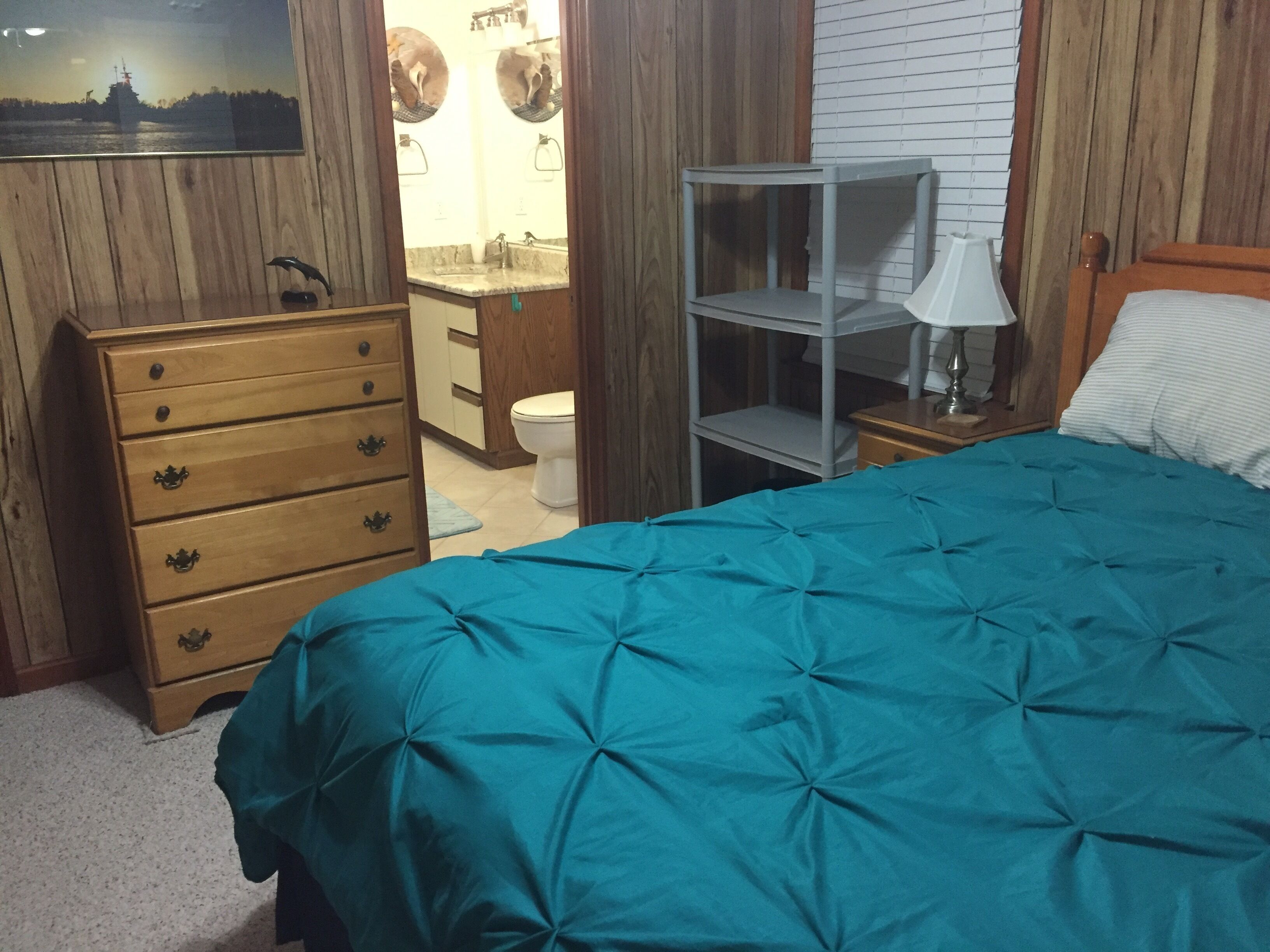 A bedroom with a bed, a dresser, a nightstand, a mirror, and a bathroom visible through an open door.