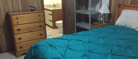 A bedroom with a bed, a dresser, a nightstand, a mirror, and a bathroom visible through an open door.