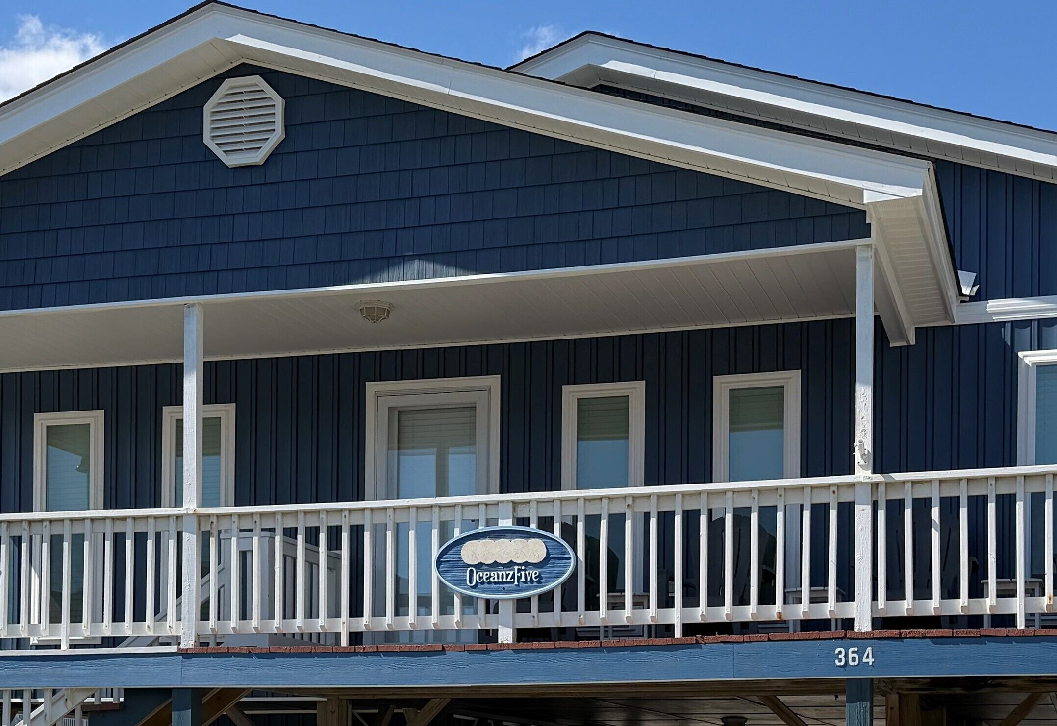 A dark blue building with a white balcony railing, a sign reading 'Oceanzive,' and the number '364' below the railing.