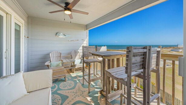 A balcony with a ceiling fan, wooden chairs, a table, and a view of the ocean. - Semi-Oceanfront Condo w/ Resort Pool, Elevator, Private Sundeck. Top Notch Stay! (Rodanthe)