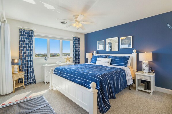 A bedroom with a bed, bedside tables, a ceiling fan, and a view of the outside. - Semi-Oceanfront Condo w/ Resort Pool, Elevator, Private Sundeck. Top Notch Stay! (Rodanthe)