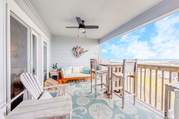 Enjoy the ocean view from this spacious balcony with a sofa, chairs, and ceiling fan.