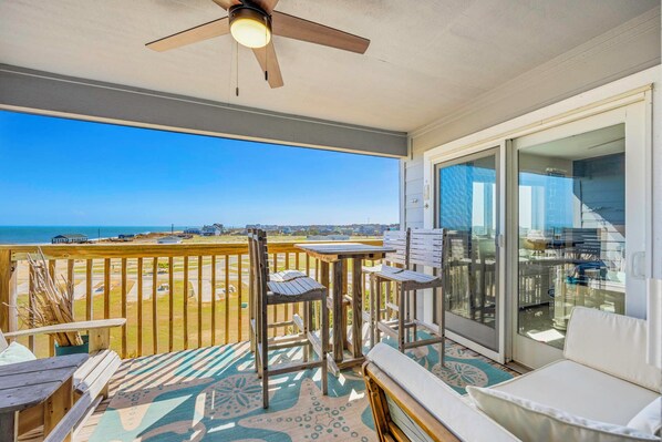 Ein Balkon mit Deckenventilator, Blick auf den Strand und eine Schiebetür zu einem Zimmer.