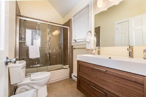 A modern bathroom with a glass-enclosed shower, a toilet, a vanity with a mirror, and a bathtub.
