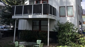 Un edificio a più piani con balconi, un'area giardino con sedie e uno sfondo montuoso.