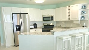 A modern kitchen with white cabinetry, stainless steel appliances, a granite countertop, and a central island with bar stools. - YOU'VE Arrived! Beachfront 3BR condo w/ Pool-Relax... North Side near Rum Point (Old Man Bay)