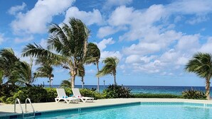 A clear blue pool with lounge chairs and palm trees, surrounded by a landscaped area. - YOU'VE Arrived! Beachfront 3BR condo w/ Pool-Relax... North Side near Rum Point (Old Man Bay)