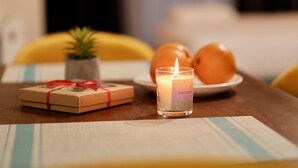 A candle labeled "Manamo" on a table with a gift box and oranges. - GUDASKI Apartments (Kazbegi)