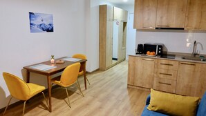 A compact living space with a dining area, kitchenette, and a sofa. - GUDASKI Apartments (Kazbegi)