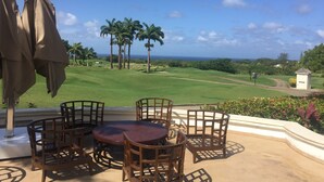 A patio with a round table and chairs, overlooking a golf course with palm trees and a view of the ocean. - Royal Westmoreland - Mahogany Drive 8 by Island Villas (Westmoreland)
