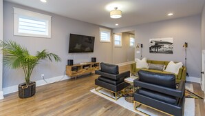 Ein modernes Wohnzimmer mit einem Flachbildfernseher, einer Holz-Unterhaltungseinrichtung, schwarzen Ledersofas und einem grünen Sessel.