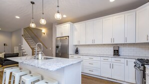 Eine moderne Küche mit weißen Schränken, einem Edelstahl-Kühlschrank, einem eingebauten Backofen und einer Marmor-Kochinsel mit Barhocker.