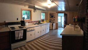 A kitchen with a stove, sink, and cabinets. There is a window above the sink and a door leading to another room. - Access to the best white sand beach in the Keweenaw! (Gay)
