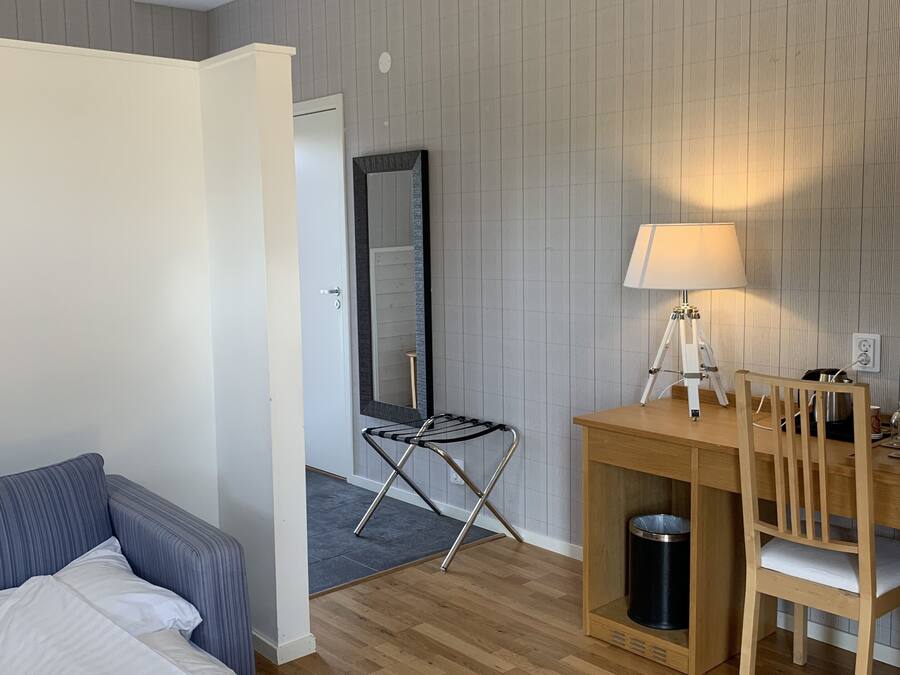 A hotel room with a wooden floor, a bed with white linens, a blue-striped sofa, a wooden desk with a lamp, a chair, and a mirror.