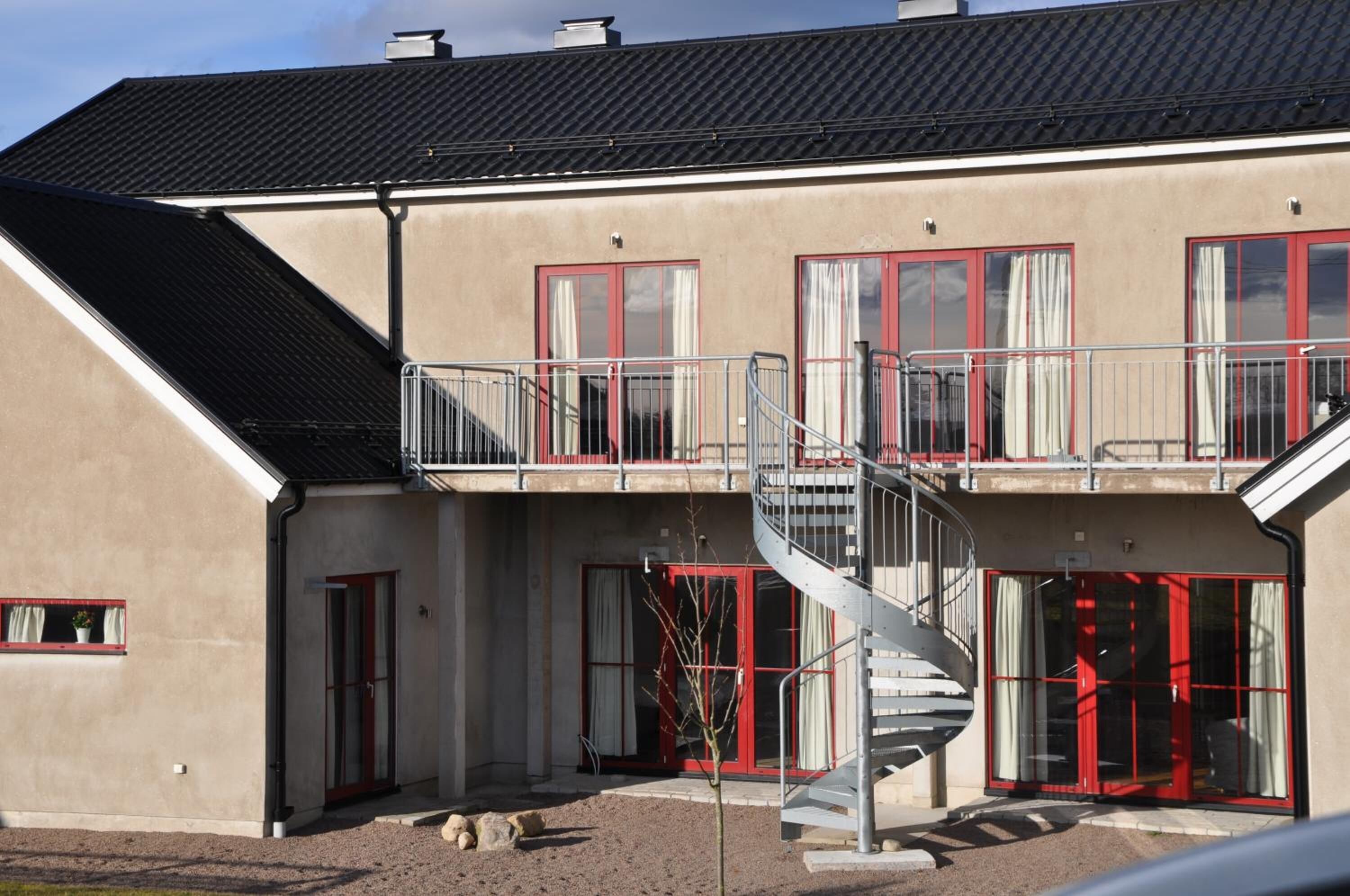 Ein zweistöckiges Gebäude mit Wendeltreppe, roten Fensterrahmen und einer beige farbenen Fassade.