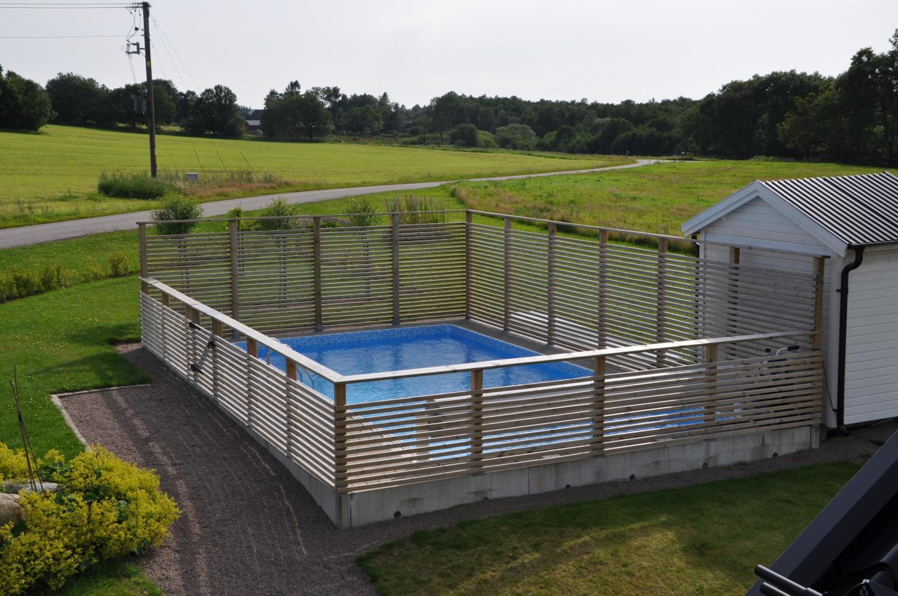 Ein rechteckiger Pool mit Holzzaun, umgeben von einer Wiese und einem kleinen Schuppen.