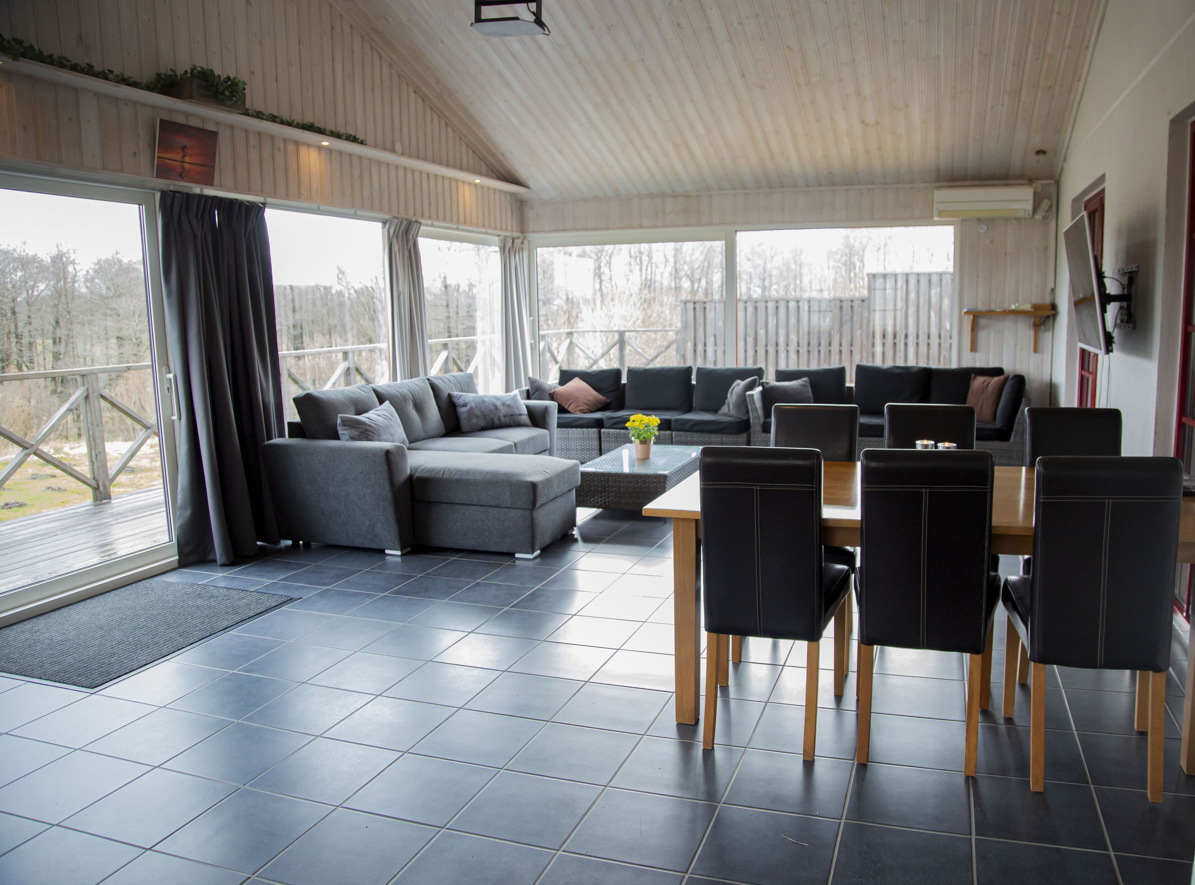 A modern living room with a sectional sofa, a dining table with chairs, and a view of the outdoors.