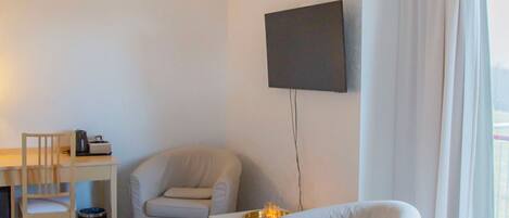A room with a wooden floor, a desk with a chair, a television mounted on the wall, and a window with curtains.