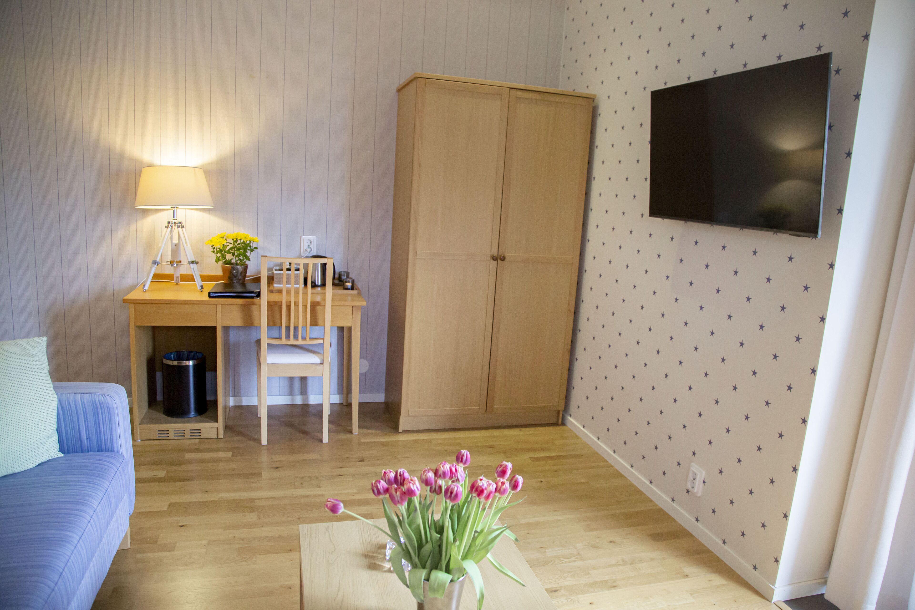 Una habitación con cama, escritorio con lámpara, armario y televisor en la pared.