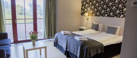 Habitación de hotel con cama, mesitas de noche, una pequeña mesa con un florero y vistas a través de un ventanal.