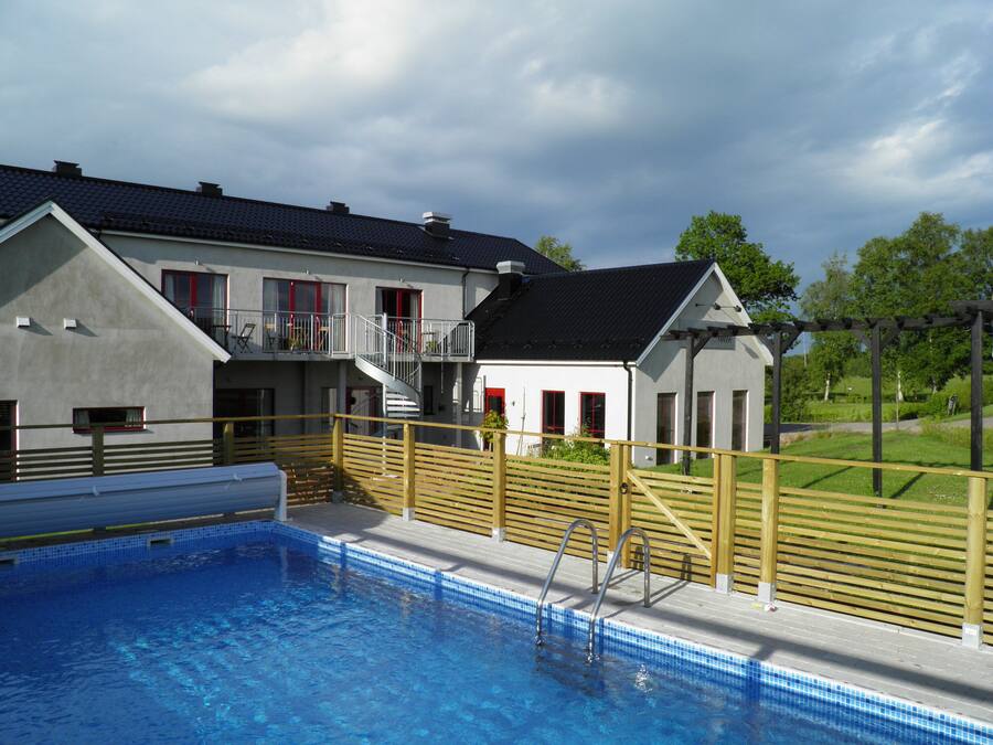 Een gebouw met twee verdiepingen, een zwembad, een houten omheining en een tuin.
