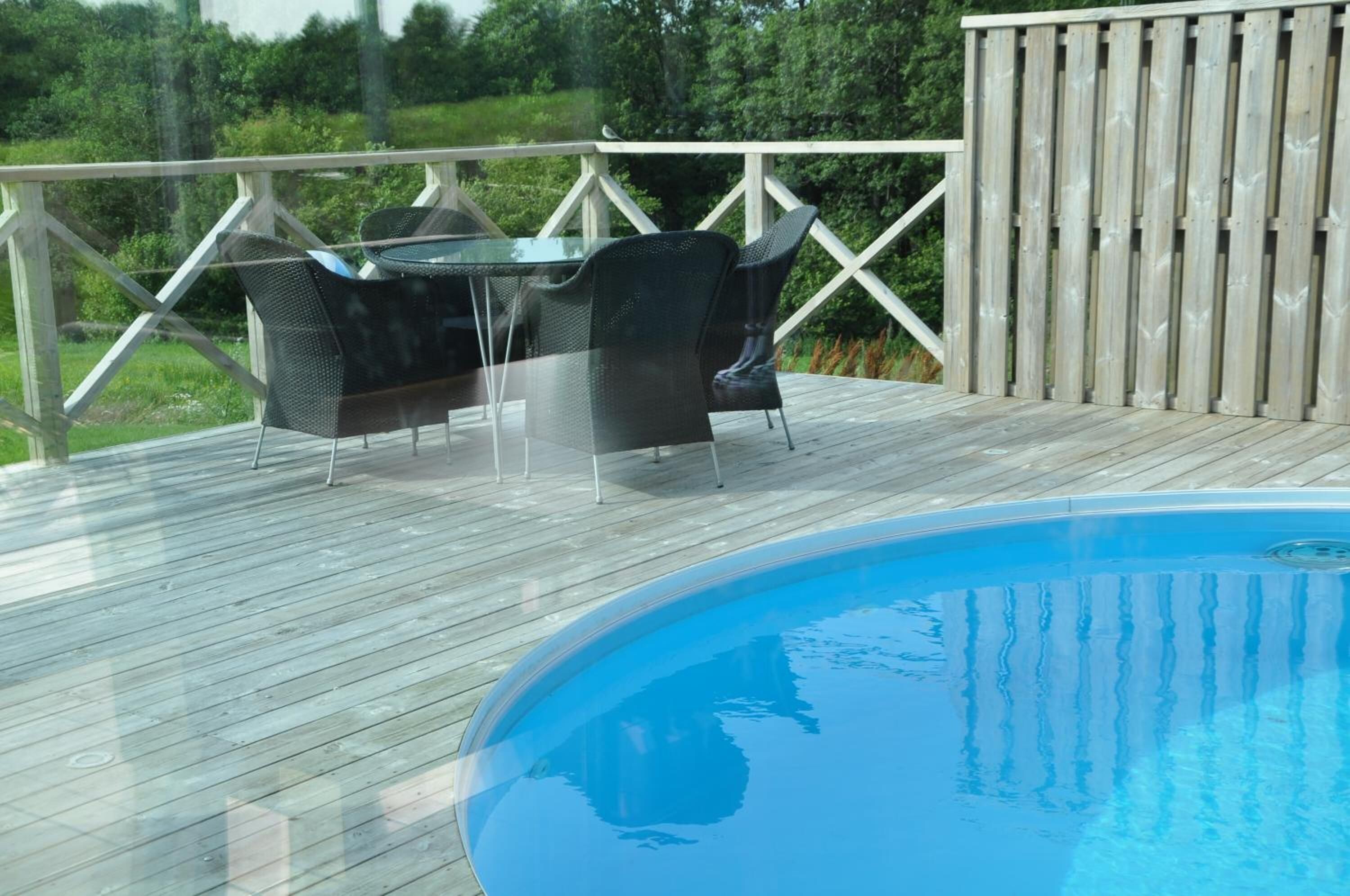 Une terrasse en bois avec une piscine, du mobilier d’extérieur et une clôture en bois.