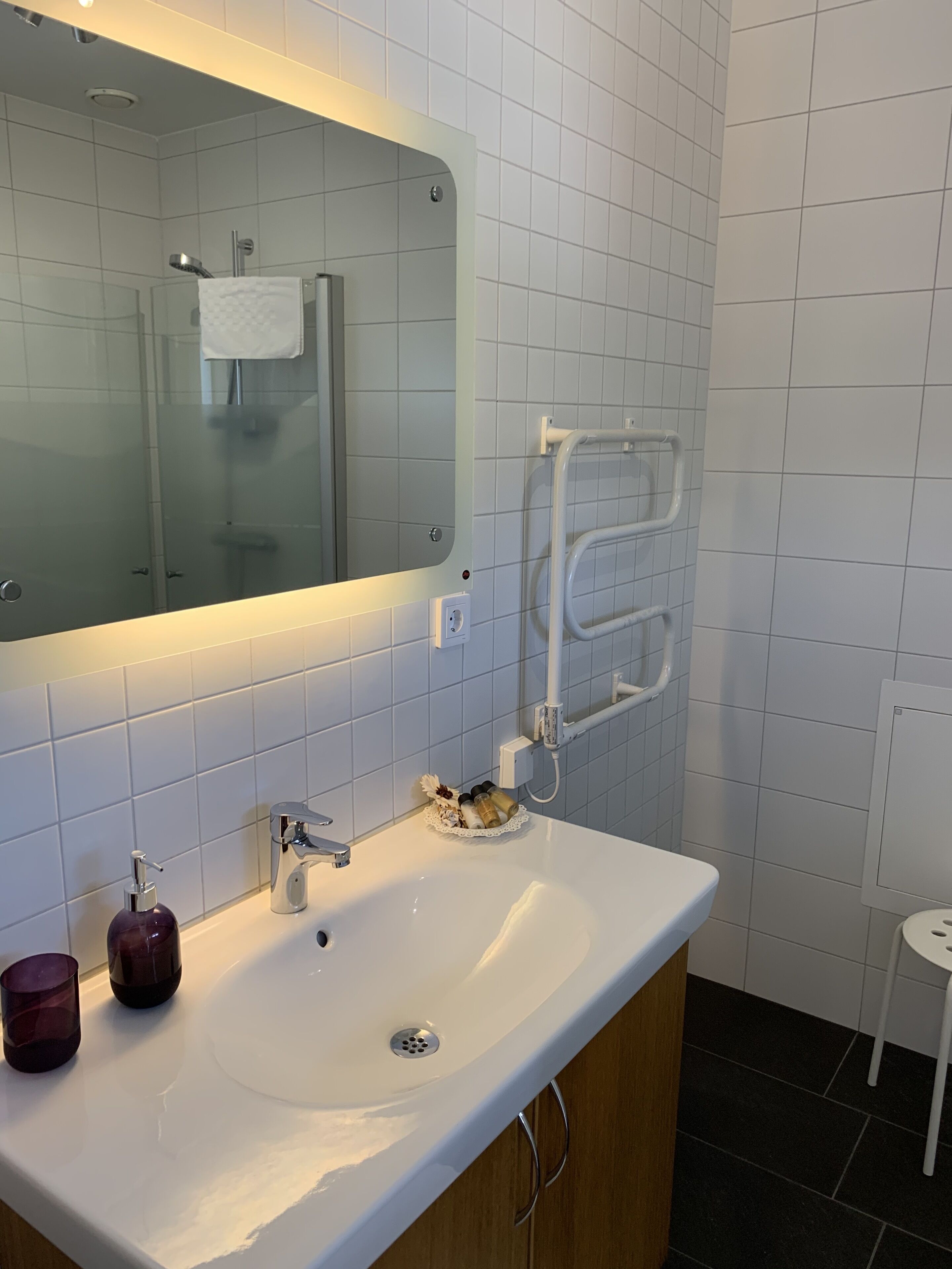 A bathroom with a white sink, a mirror, a towel rack, and a small stool.
