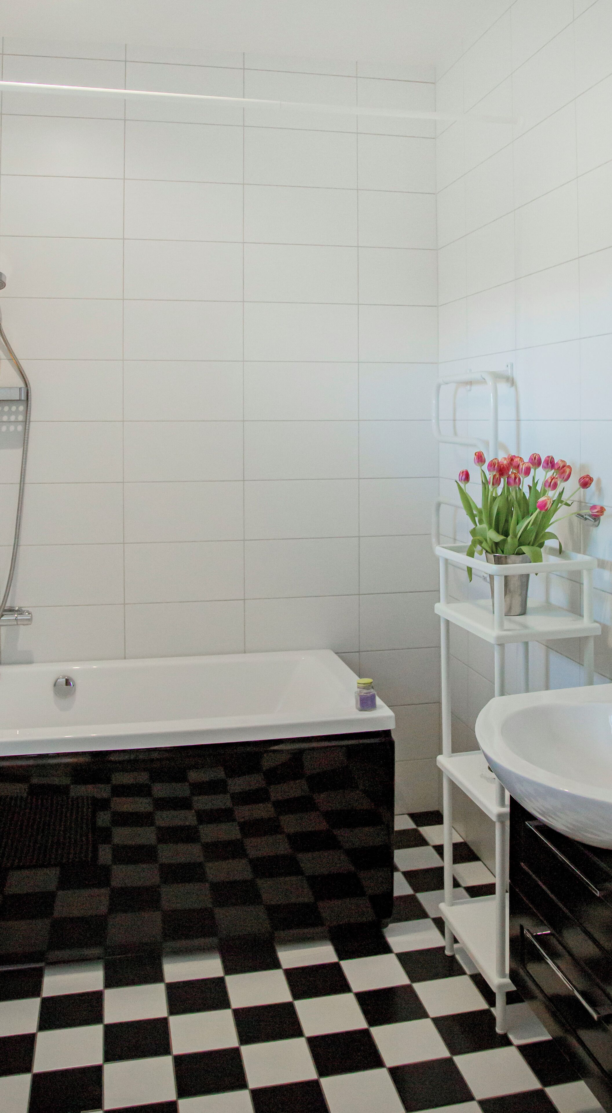 A bathroom with a bathtub, a white sink, and a shelf with flowers.