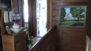 A wooden interior with a staircase, a wooden cabinet with a mirror, a vase with flowers, and a framed painting on the wall. - Relax in a Peaceful Country Home in the Blue Ridge Mountains. Enjoy Local Events (Sparta)