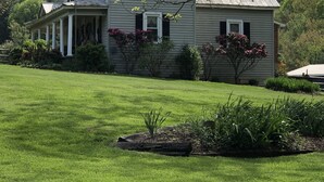 A two-story house with a porch, surrounded by a well-maintained lawn and flowering shrubs. - Relax in a Peaceful Country Home in the Blue Ridge Mountains. Enjoy Local Events (Sparta)