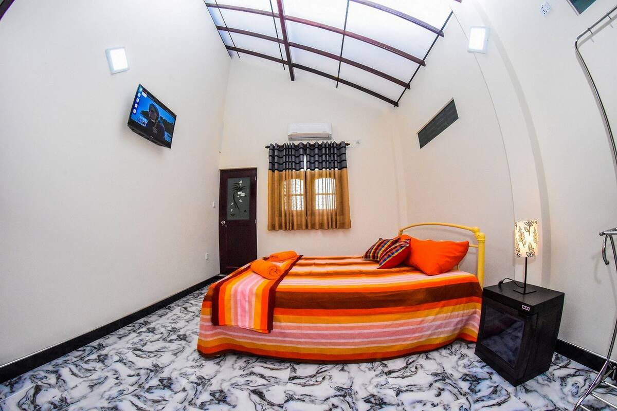 A bedroom with a bed, a TV, an air conditioning unit, and a window with curtains.