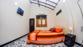 Un dormitorio con cama, televisor, equipo de aire acondicionado y ventana con cortinas.