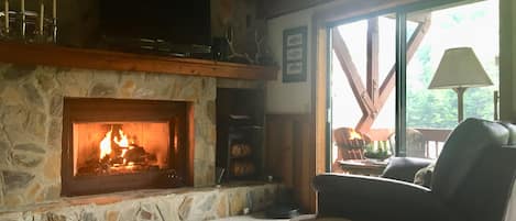 A cozy living room with a stone fireplace, a television mounted above it, and a comfortable seating area with a chair and a small table.