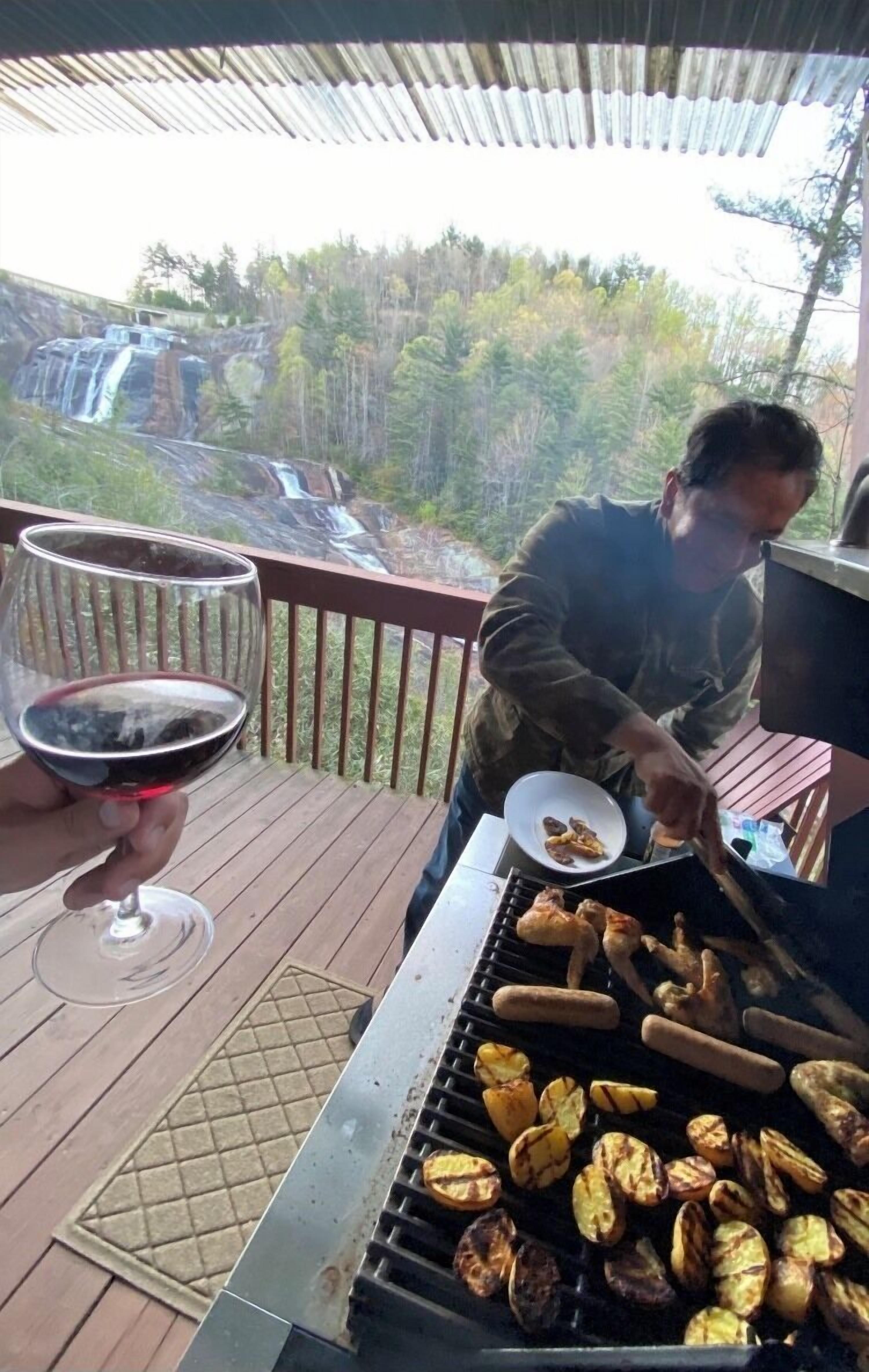 A person grilling food on an outdoor grill with a scenic view of a waterfall in the background.