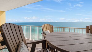 A balcony with a view of the ocean, featuring a table and two Adirondack chairs. - Tropic Winds 1504 - Amazing beachfront condo! Beach chairs included! (Panama City Beach)