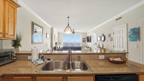 A kitchen with granite countertops, stainless steel sinks, wooden cabinets, and a ceiling fan. - Tropic Winds 1504 - Amazing beachfront condo! Beach chairs included! (Panama City Beach)