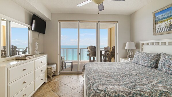 A bedroom with a bed, dresser, TV, and a balcony with chairs and a table. - Tropic Winds 1504 - Amazing beachfront condo! Beach chairs included! (Panama City Beach)