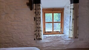 Una habitación con pared de piedra, ventana de madera y cortinas con estampado de hojas.