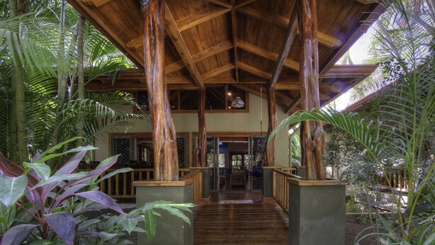 A wooden covered walkway leading to a building with a high ceiling and large windows. - Family Oasis Minutes Walk to the Playa Guiones (Nosara)