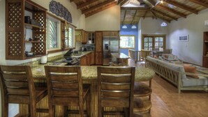 A spacious kitchen with wooden cabinets, a granite countertop, and a dining area with wooden chairs and a sofa. - Family Oasis Minutes Walk to the Playa Guiones (Nosara)