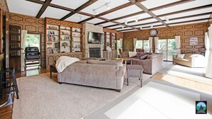 Een ruime woonkamer met een open haard, comfortabele zithoeken, een televisie en een boekenkast.