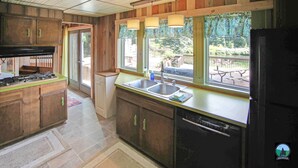 Een keuken met houten kastjes, een spoelbak en een raam met uitzicht op een terras.