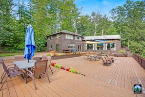 A wooden deck with outdoor furniture, a covered seating area, and a house with a large window overlooking the deck.