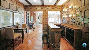 Een bar met houten lambrisering, barstoelen en ingelijste foto's aan de wand.